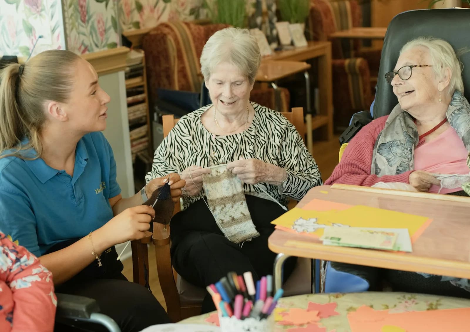 A carer sitting alongside two older women in a comfortable lounge — the lived reality of long-term care at home that a Care Act needs assessment is designed to recognise, support, and fund.