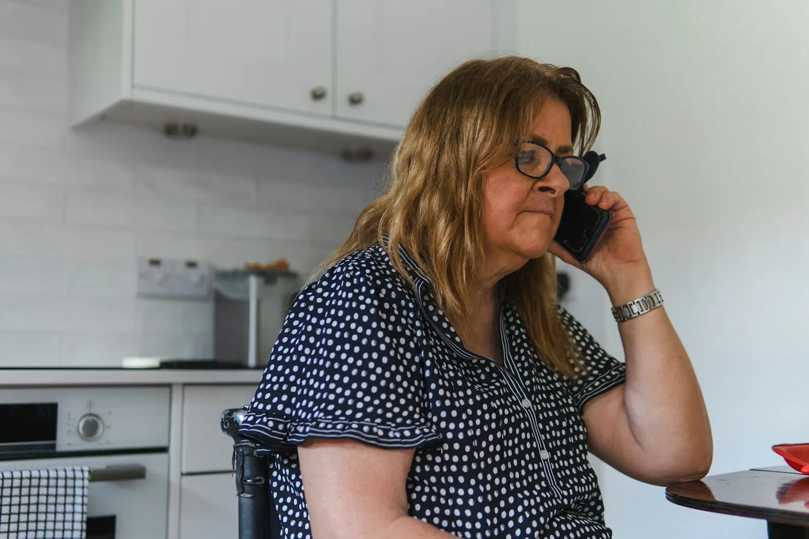 A woman on the phone in her kitchen — the practical moment of contacting the council's adult social care duty team to request a Care Act needs assessment under Section 9.