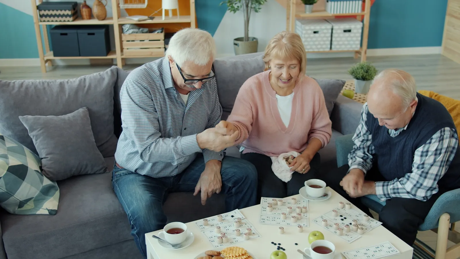 Three older residents seated together at a puzzle activity in a communal day room — the built-in social engagement that residential care home settings provide and that live-in care typically delivers through visits and external community contacts instead.