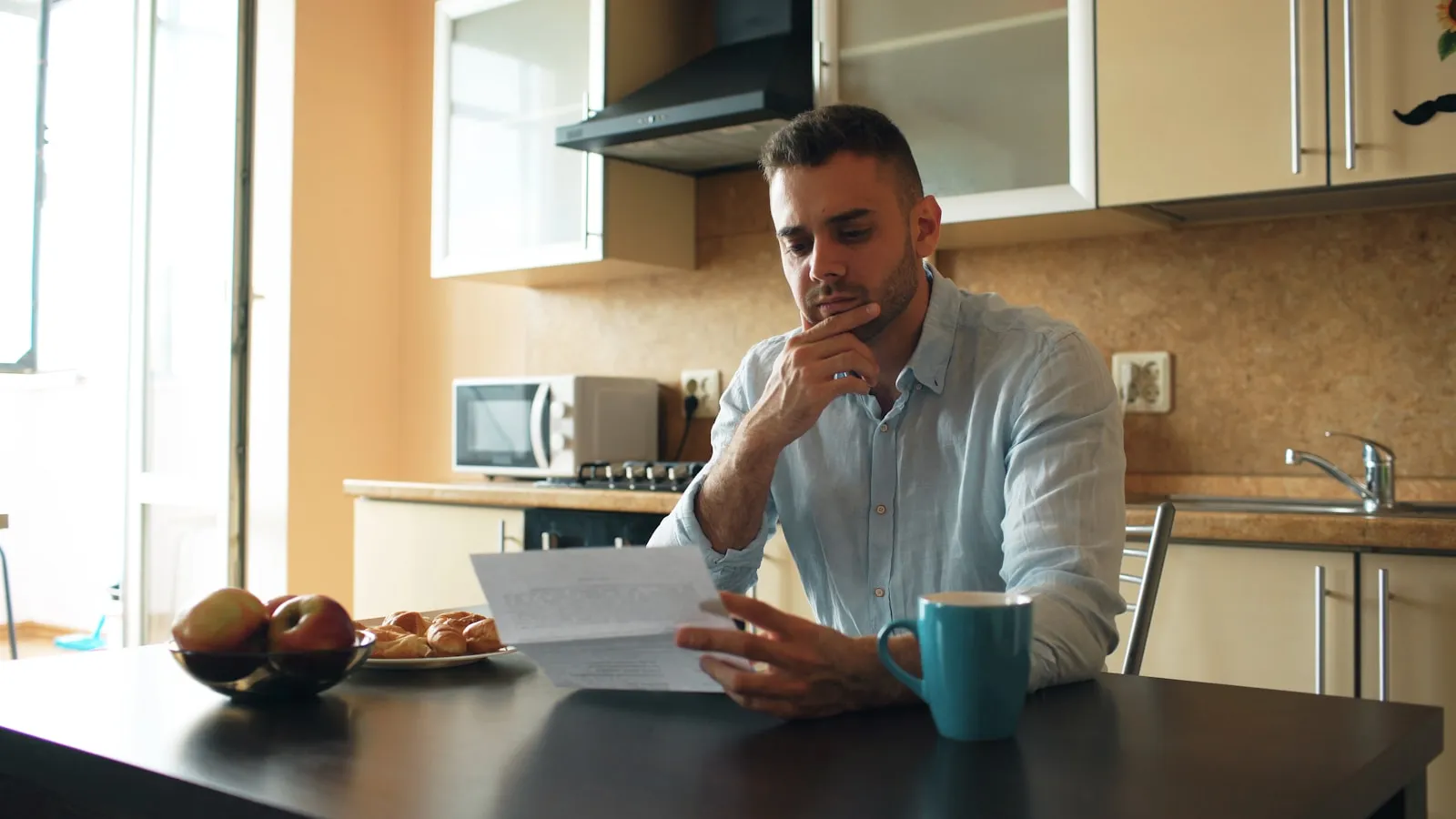 A person sitting at a kitchen table reading a DWP letter alongside a printed care diary and coffee — the typical setup for completing the DS700 Carer's Allowance application.