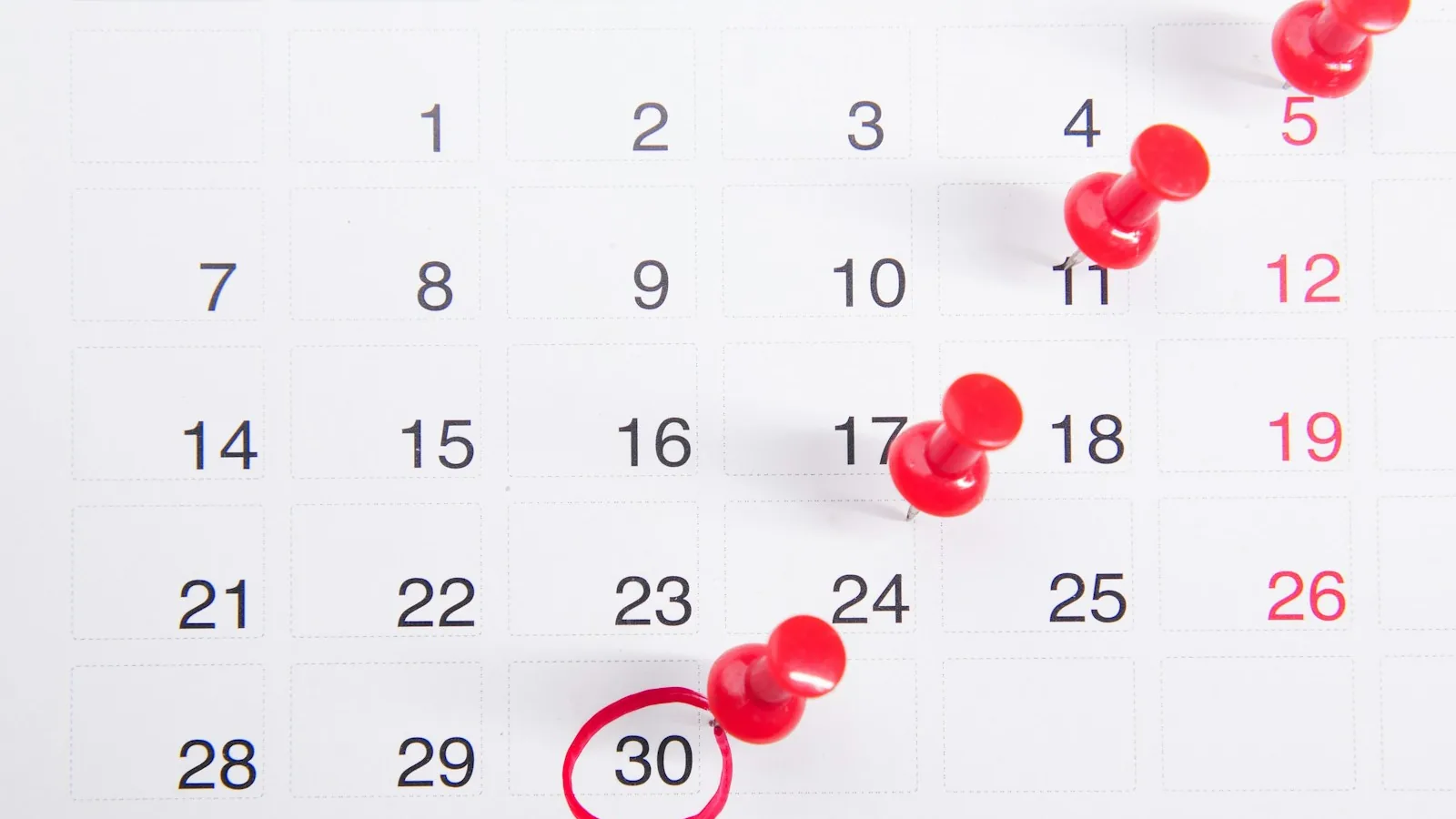 A wall calendar with red push pins marking a date — visual stand-in for the 6-month statutory deadline that starts on the date printed on an NHS Continuing Healthcare decision letter.