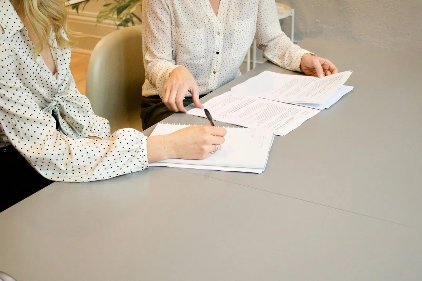 An older couple sitting at a kitchen table signing a Lasting Power of Attorney form, with reading glasses, a fountain pen, and the OPG instruction guide visible — the everyday scene of an LPA being made before any crisis.