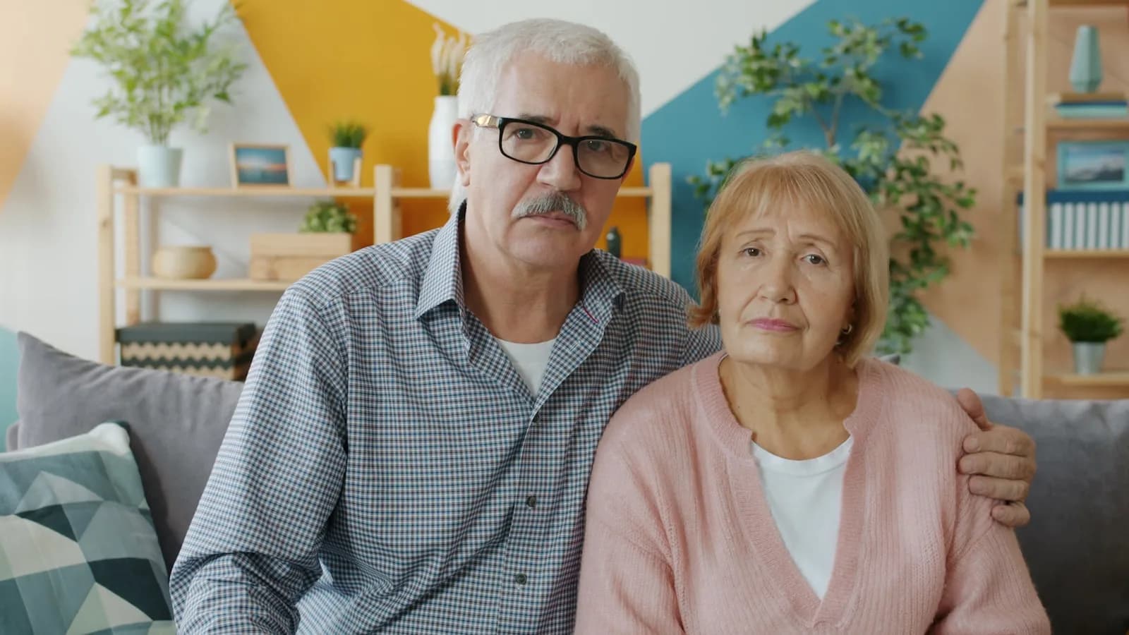 An elderly couple sitting closely together at home with concerned expressions — the moment families realise they are entering the NHS CHC funding pathway.
