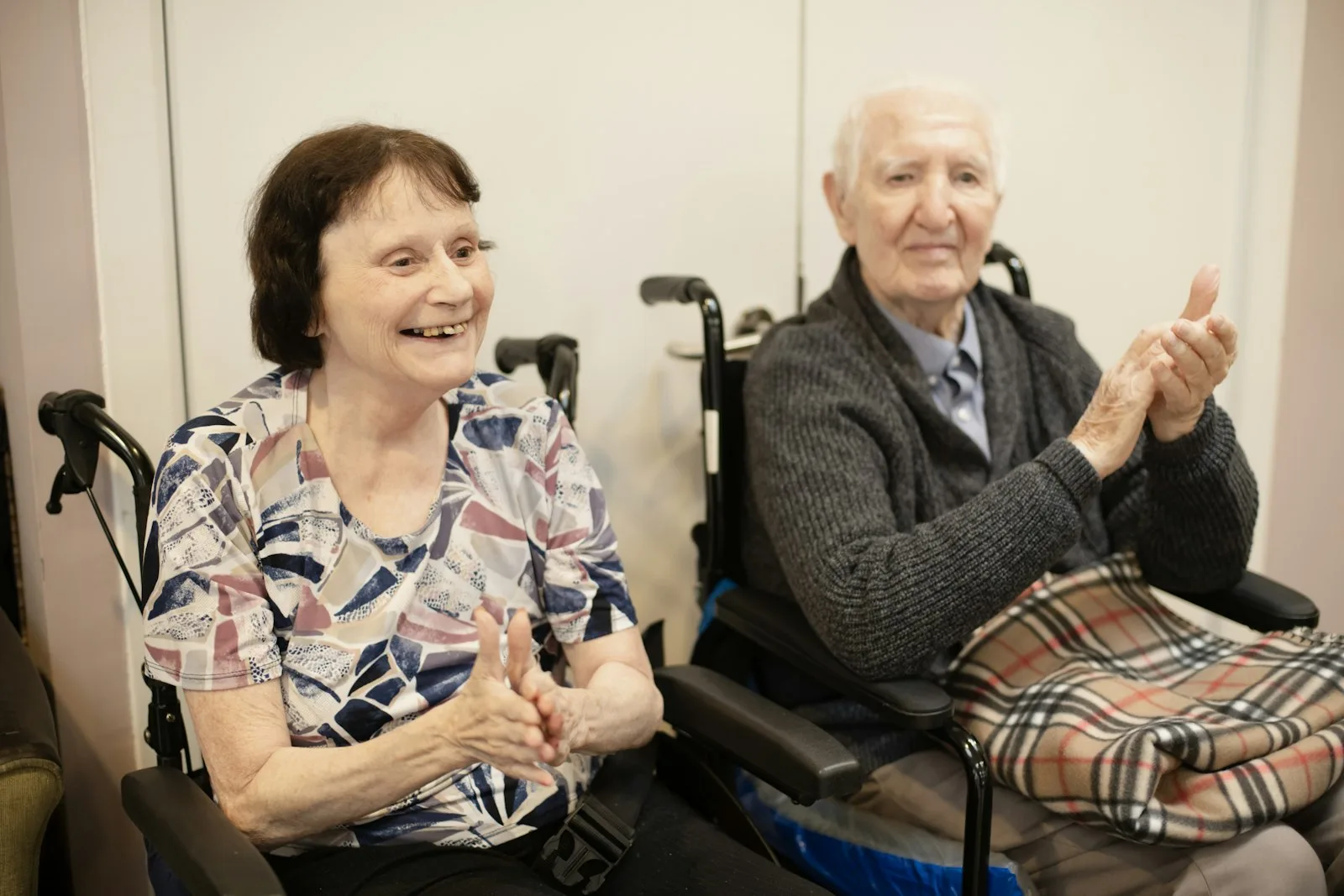 Two older care home residents sitting together in a day room, smiling and chatting — the social contact and supervision a respite stay provides for the cared-for person while the family carer takes a break.