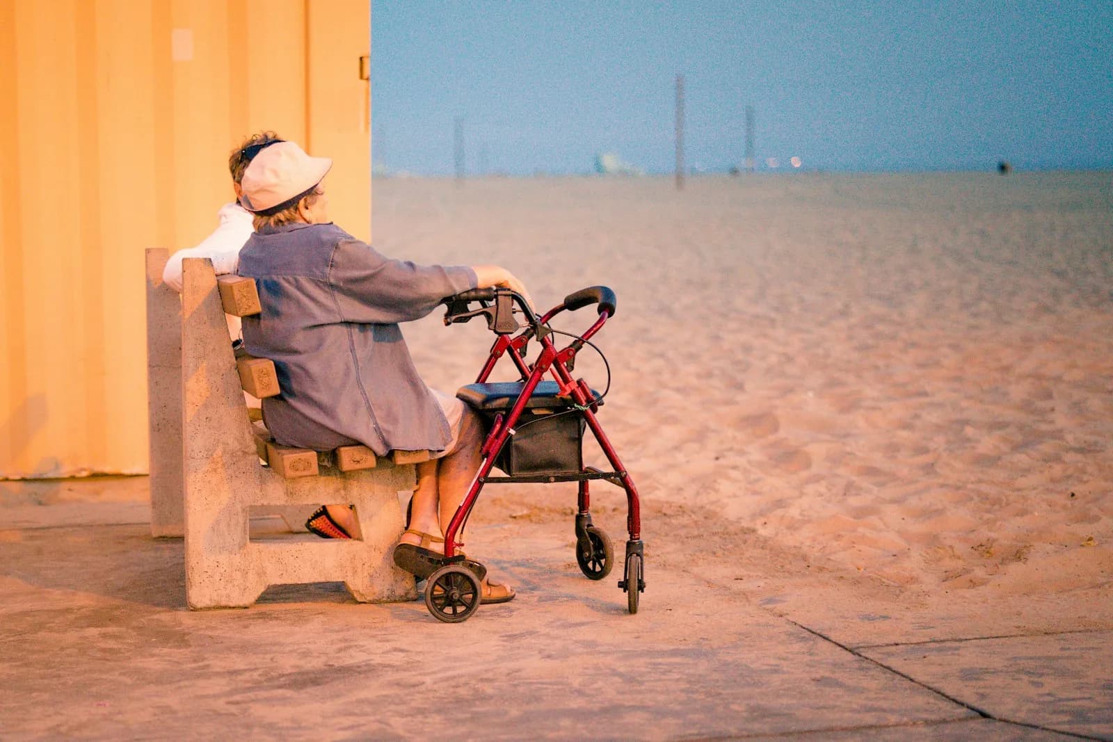 An older person sitting alone with a walker at the end of a long day, looking out across an empty space — the kind of quiet, exhausted moment that respite care exists to prevent, when it's planned early rather than left until carer breakdown.