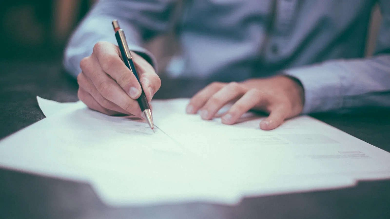 A hand writing on paperwork at a desk — drafting a structured Stage 1 Local Resolution request to challenge an NHS Continuing Healthcare refusal.