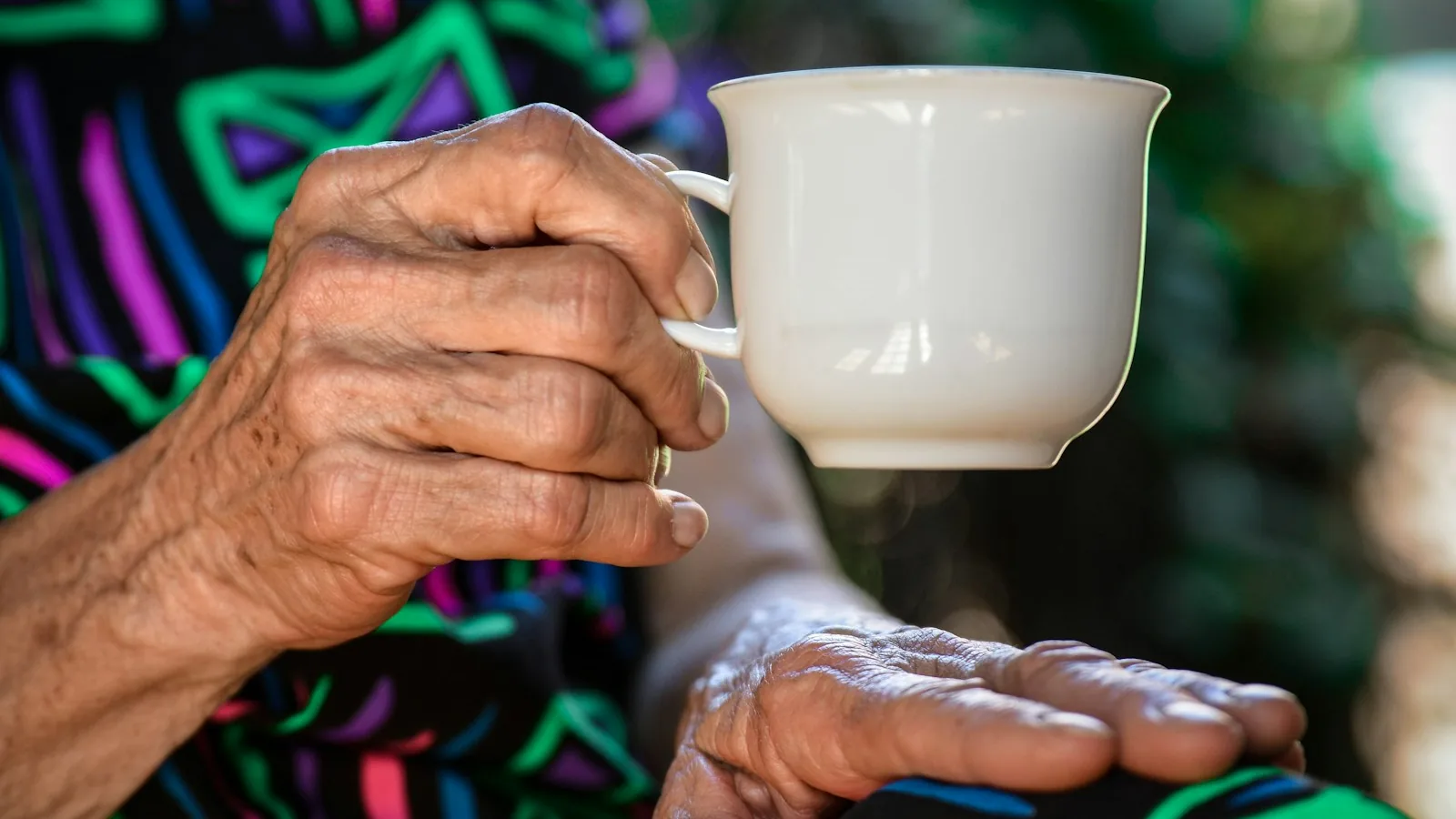 An older person holding a ceramic teacup in a warm domestic setting — UK care home funding affects every family, and most miss the option the NHS is required to assess but not required to introduce.